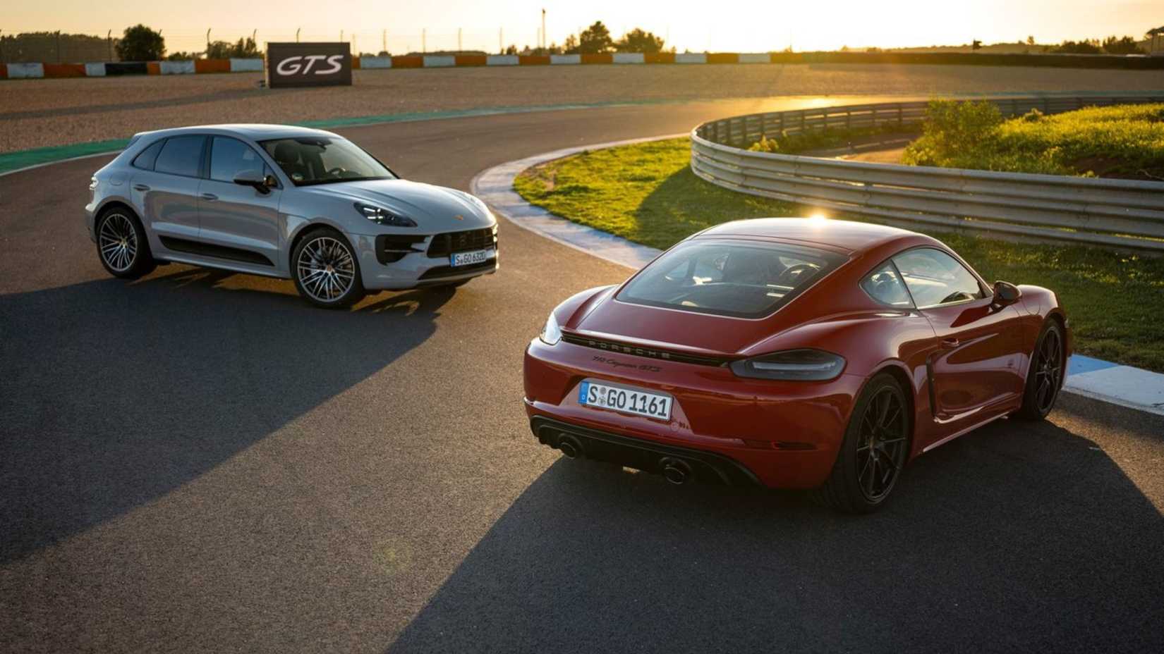 Static front 3/4 shot of a gray 2020 Porsche Macan GTS parked on a racetrack next to a red Porsche Cayman GTS.