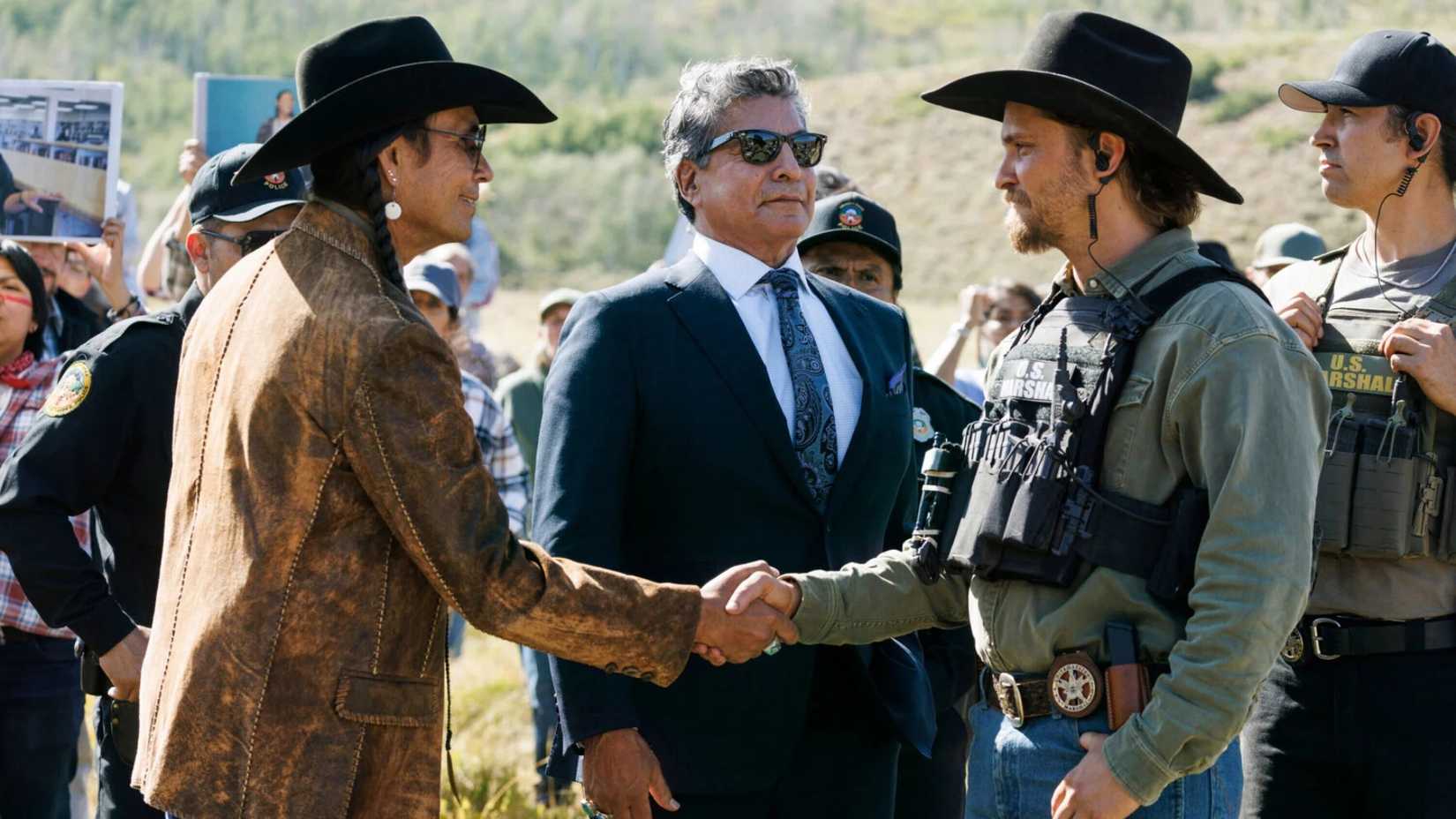 Mo Brings Plenty as Mo and Luke Grimes as Kayce Dutton shaking hands while Gil Birmingham as Thomas Rainwater looks on behind them in Marshals.