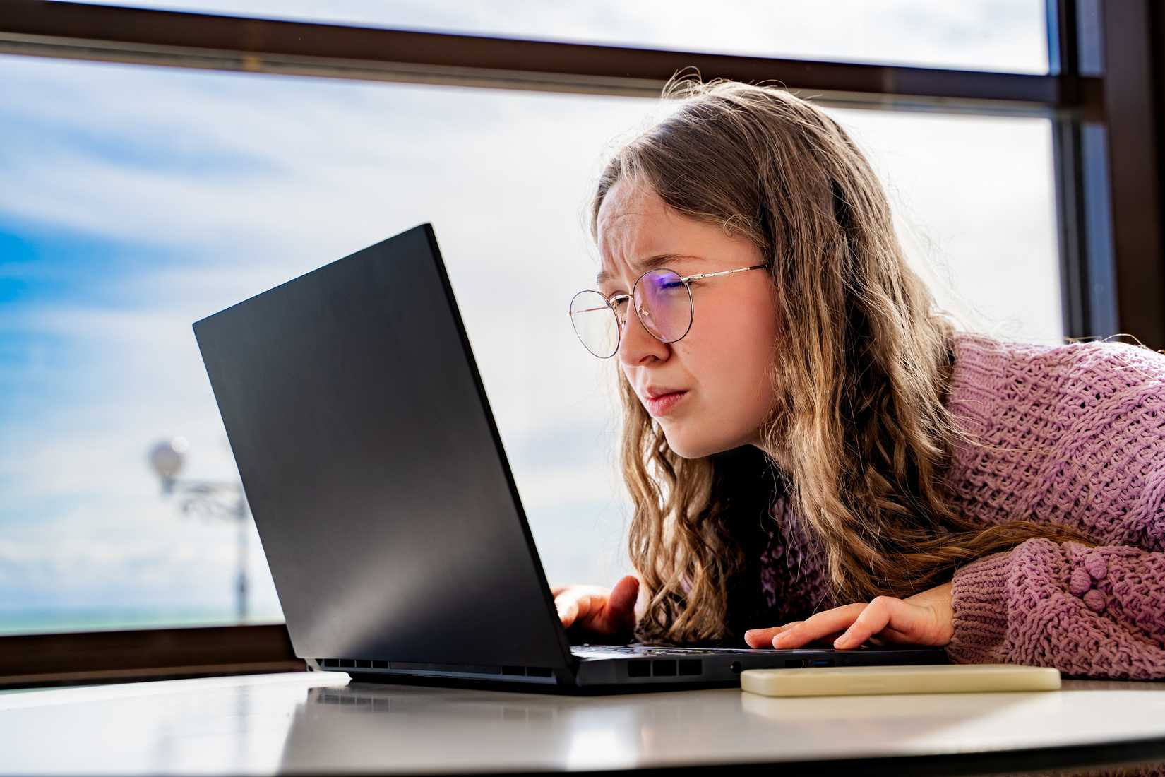 Young woman with glasses squinting at laptop screen.