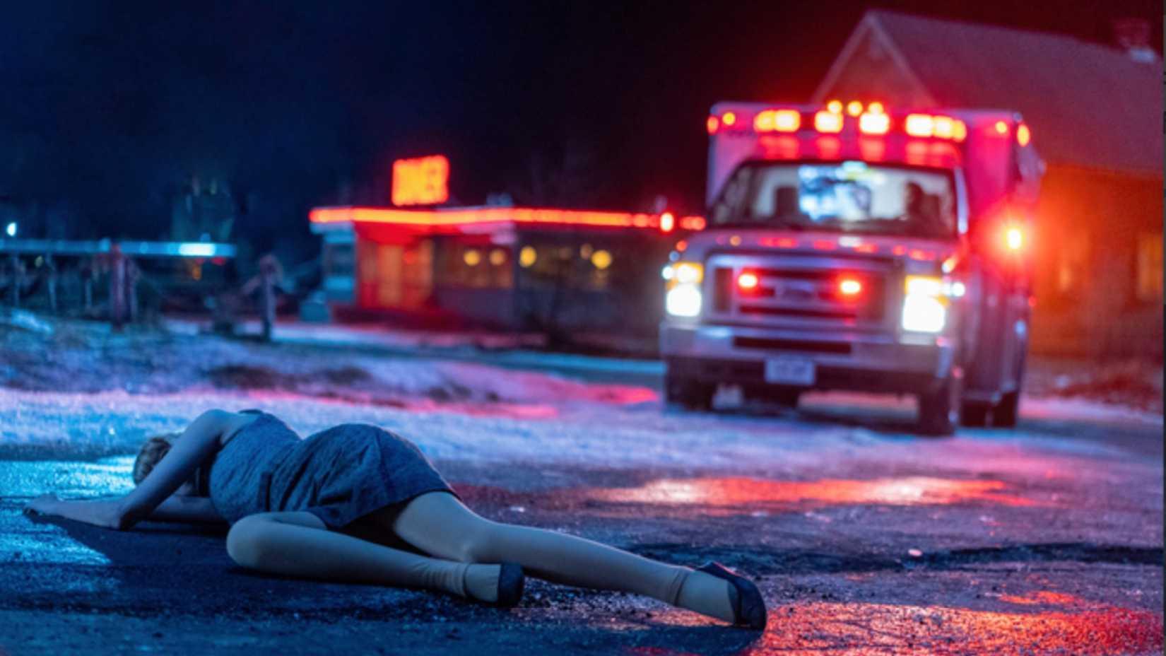 An ambulance approaches a woman lying in the street at night in From.