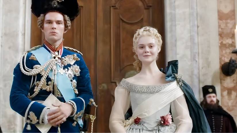 Elle Fanning and Nicholas Hoult in The Great, looking down at someone coming on stairs. 