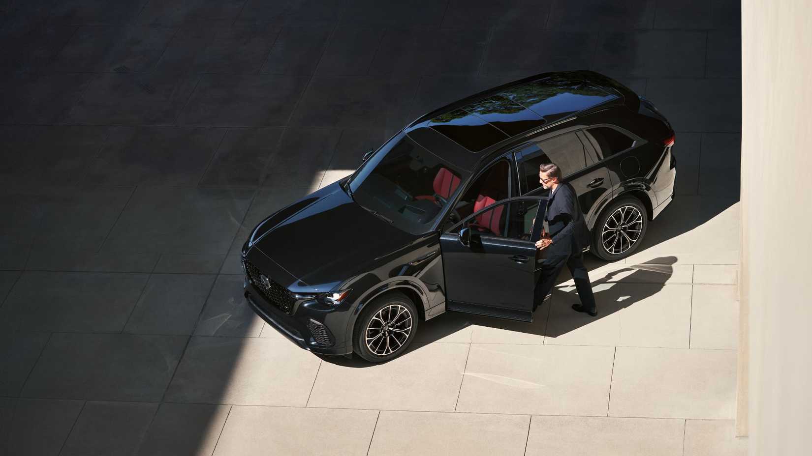 Static overhead front 3/4 shot of a man stepping into a black 2026 Mazda CX-70.
