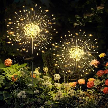 Two starburst-style solar garden lights glowing warmly among flowers in a nighttime garden setting.