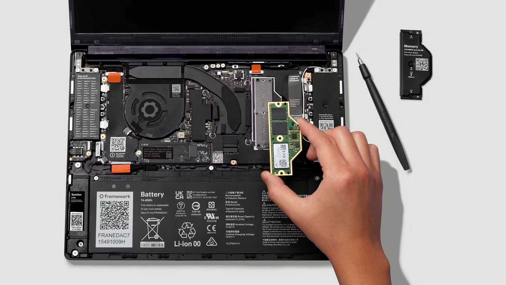 A hand holding an LPCAMM2 RAM memory module above the Framework Laptop 13 Pro.