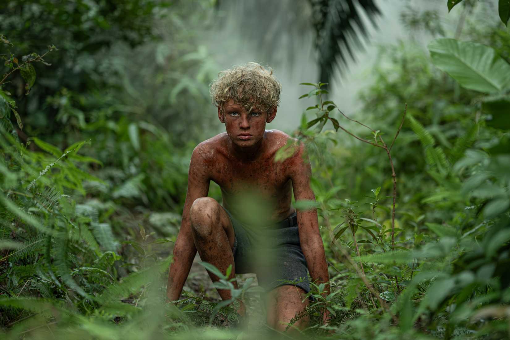 Jack from Lord of the Flies series crouched down in the jungle
