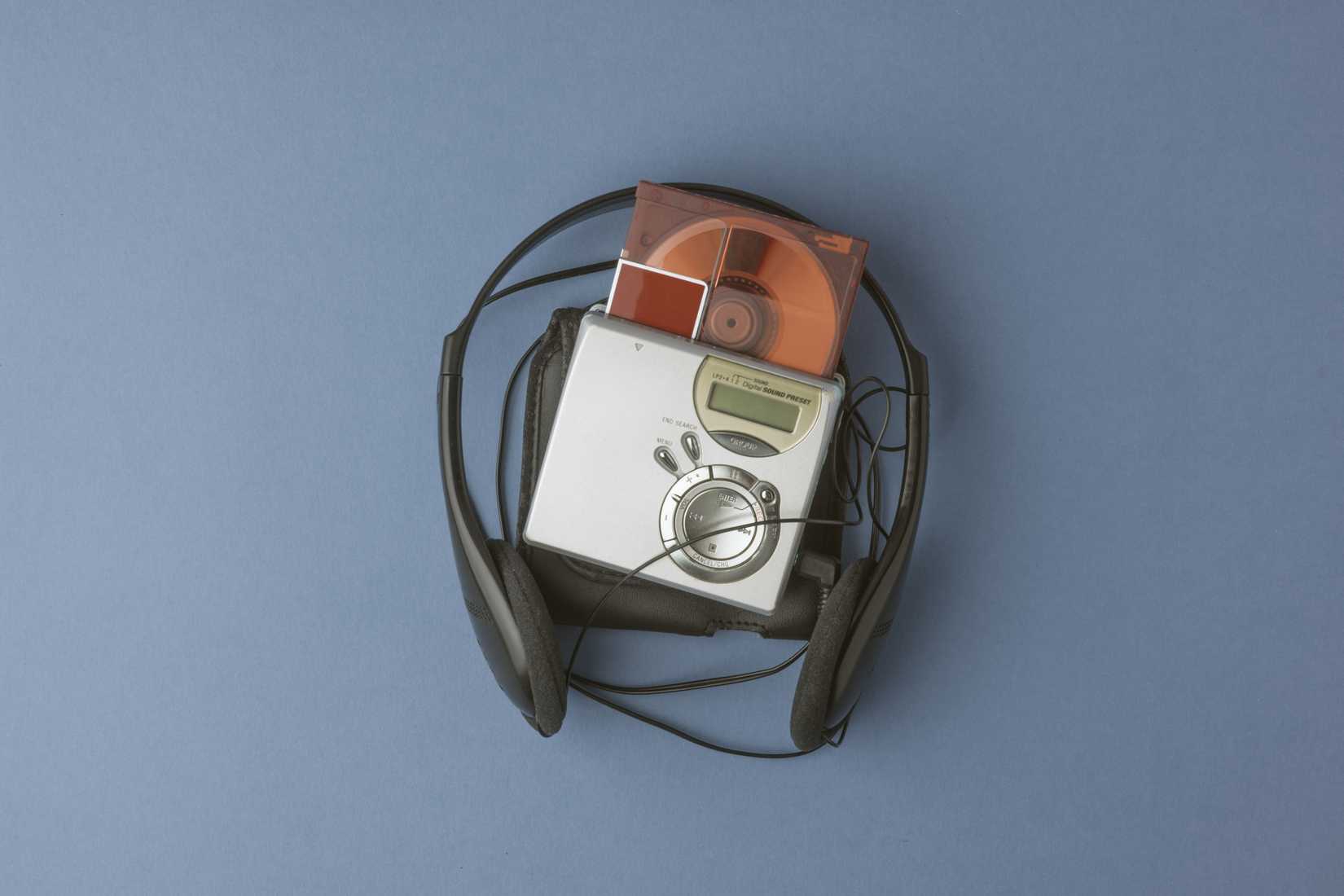 Portable MiniDisc player with a disc inserted, surrounded by wired headphones on a blue background.
