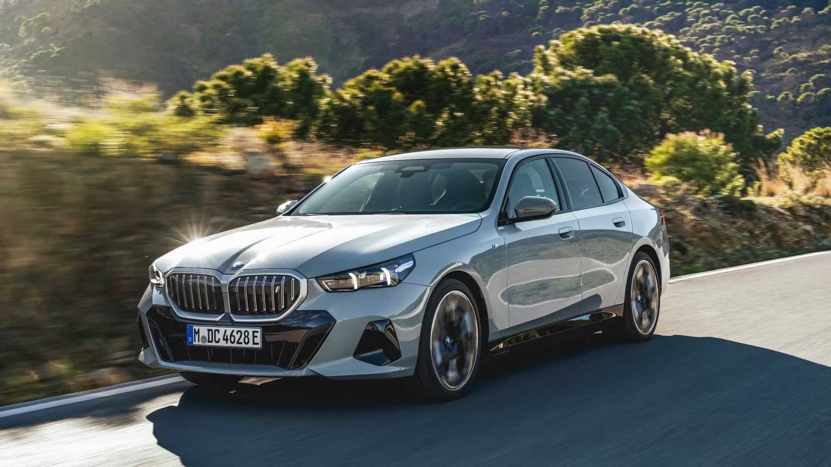Front 3/4 action shot of 2025 BMW 5 Series in silver driving on road