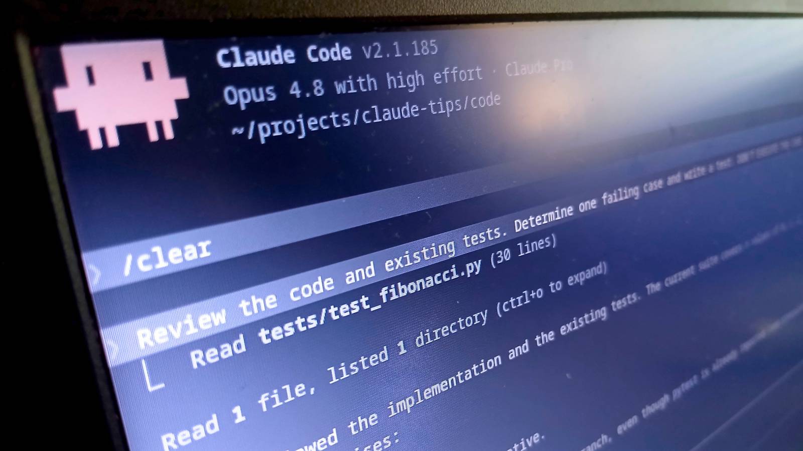A photograph of a screen at an angle showing the Claude Code welcome banner and a prompt to review the code and existing tests.