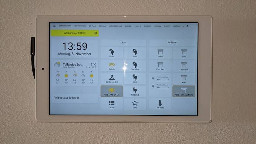 A tablet displaying a Home Assistant dashboard mounted on magnets on a wall.