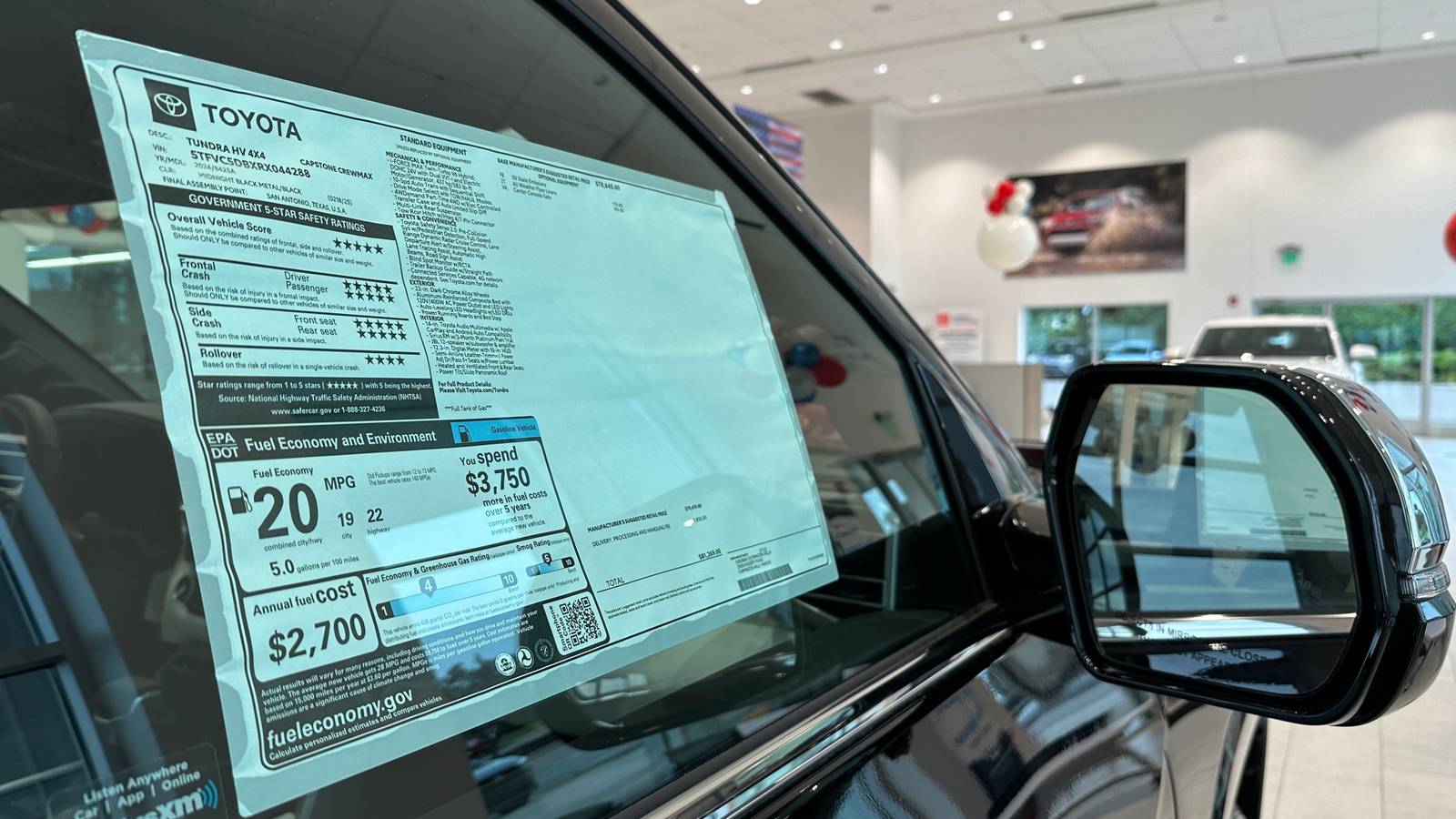 A new Toyota with a close up view of the dealership sales sticker on the window. The car is in the dealership's showroom
