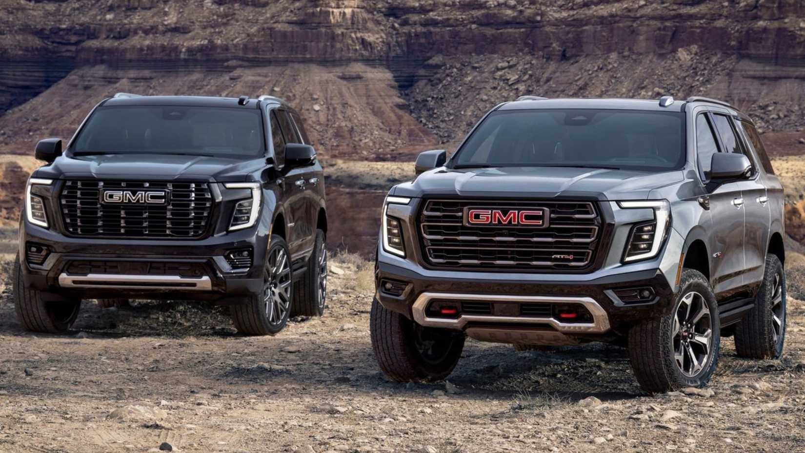 グレーの 2025 GMC ユーコン AT4 の隣にある、黒の 2025 GMC ユーコン デナリの 3/4 正面静止ショット。