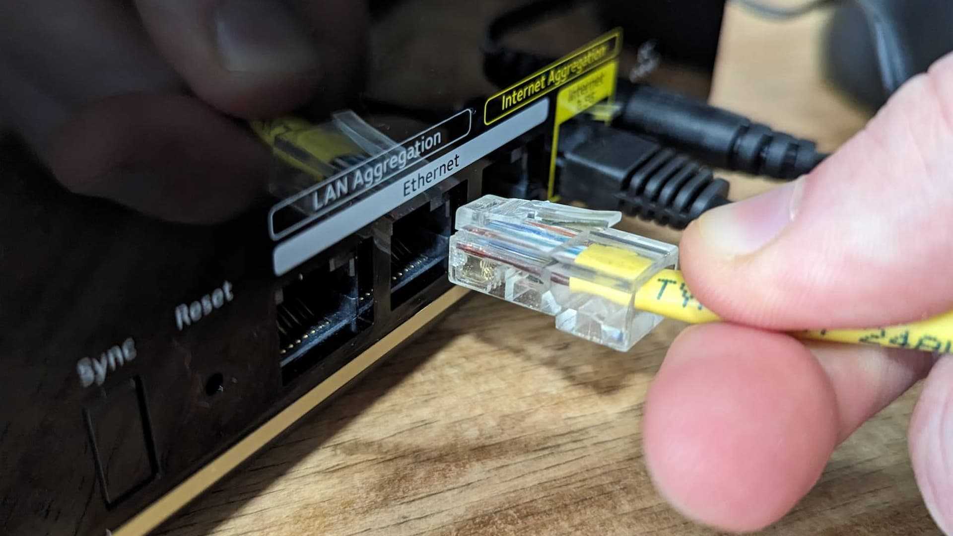 Person plugging an Ethernet cable into a port on the Netgear Nighthawk MK93S Tri-Band Mesh Wifi 6E System.
