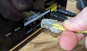 Person plugging an Ethernet cable into a port on the Netgear Nighthawk MK93S Tri-Band Mesh Wifi 6E System.