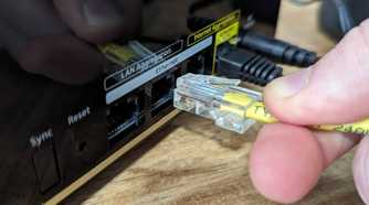 Person plugging an Ethernet cable into a port on the Netgear Nighthawk MK93S Tri-Band Mesh Wifi 6E System.
