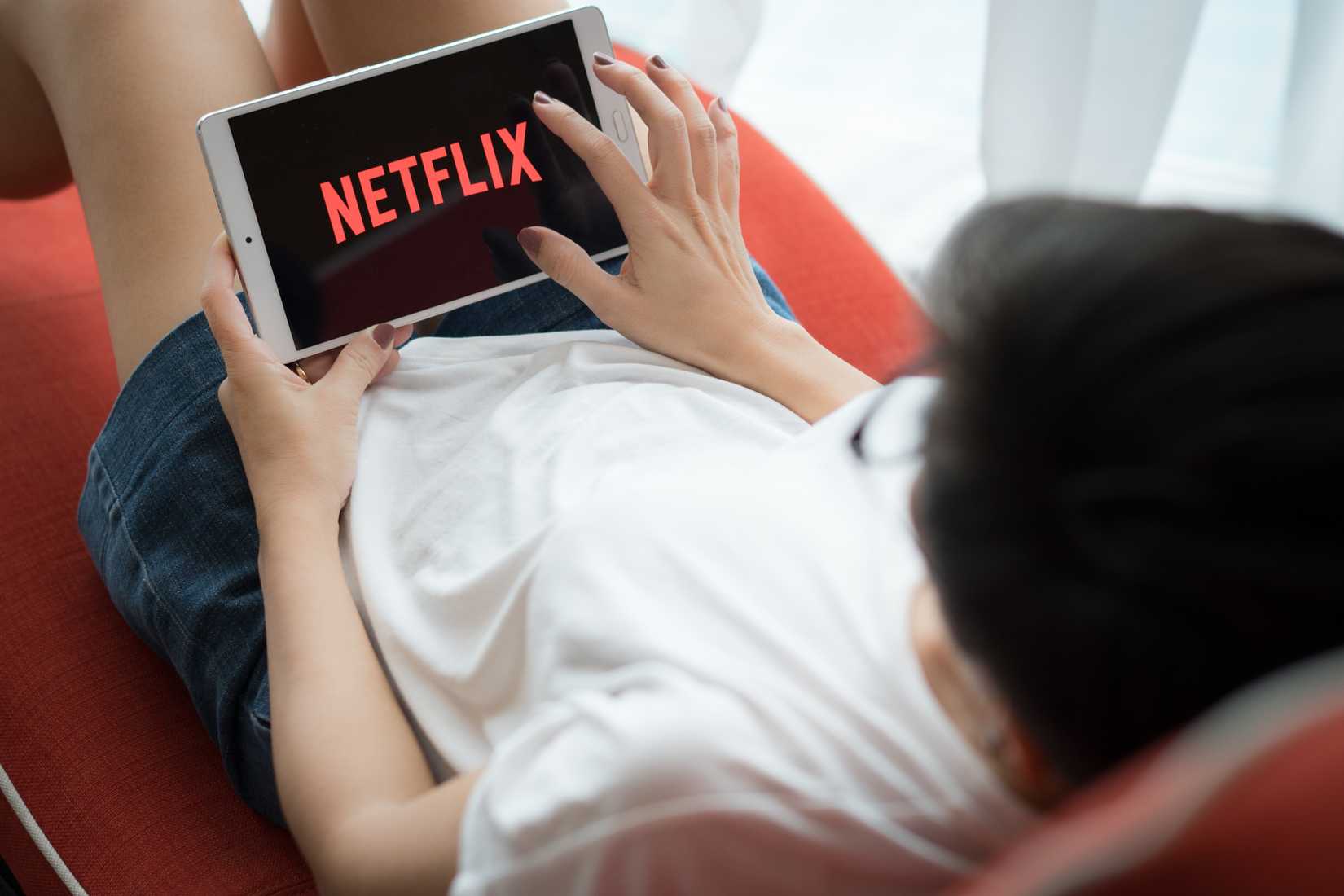 Person streaming Netflix on a tablet while relaxing on a couch.