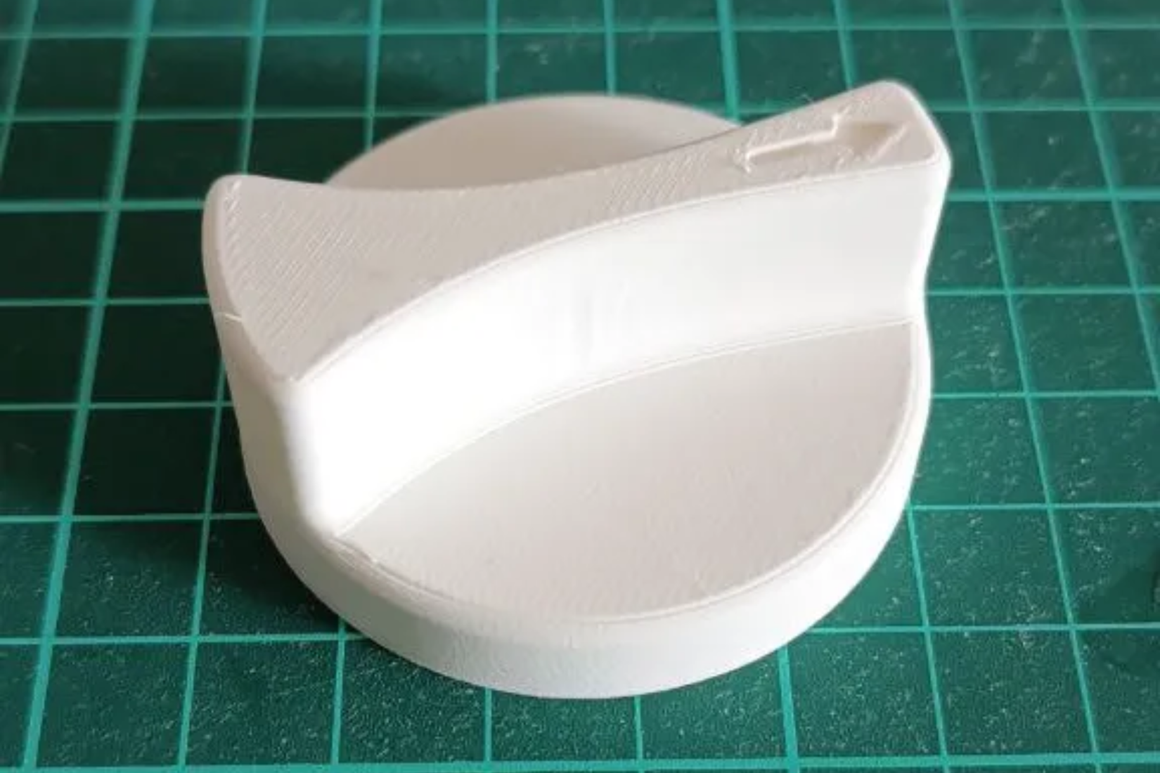 Stove knob that was 3D printed sitting on a green cutting mat.