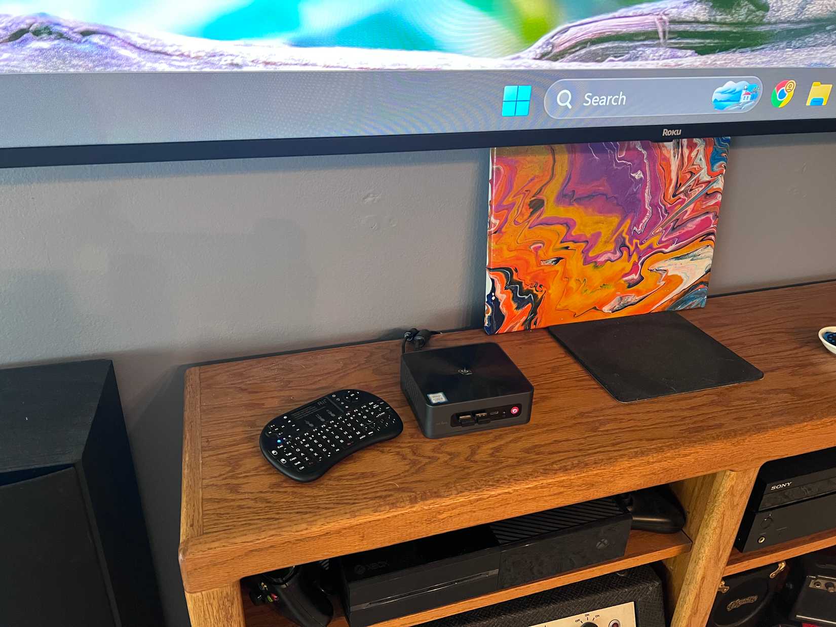An image of mini PC on a shelving unit under a TV/computer monitor.