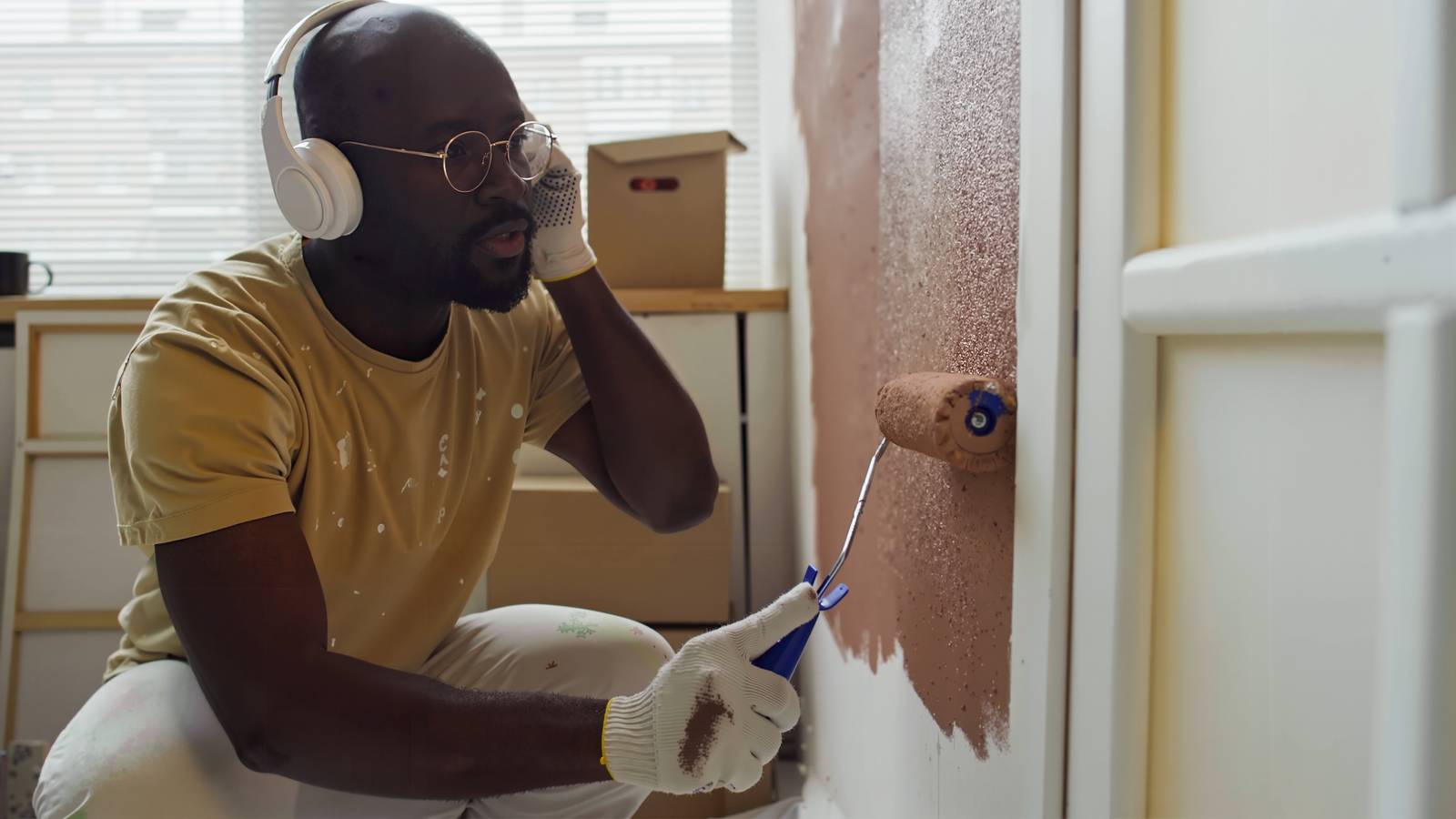A man wearing headphones paints a wall with a paint roller.