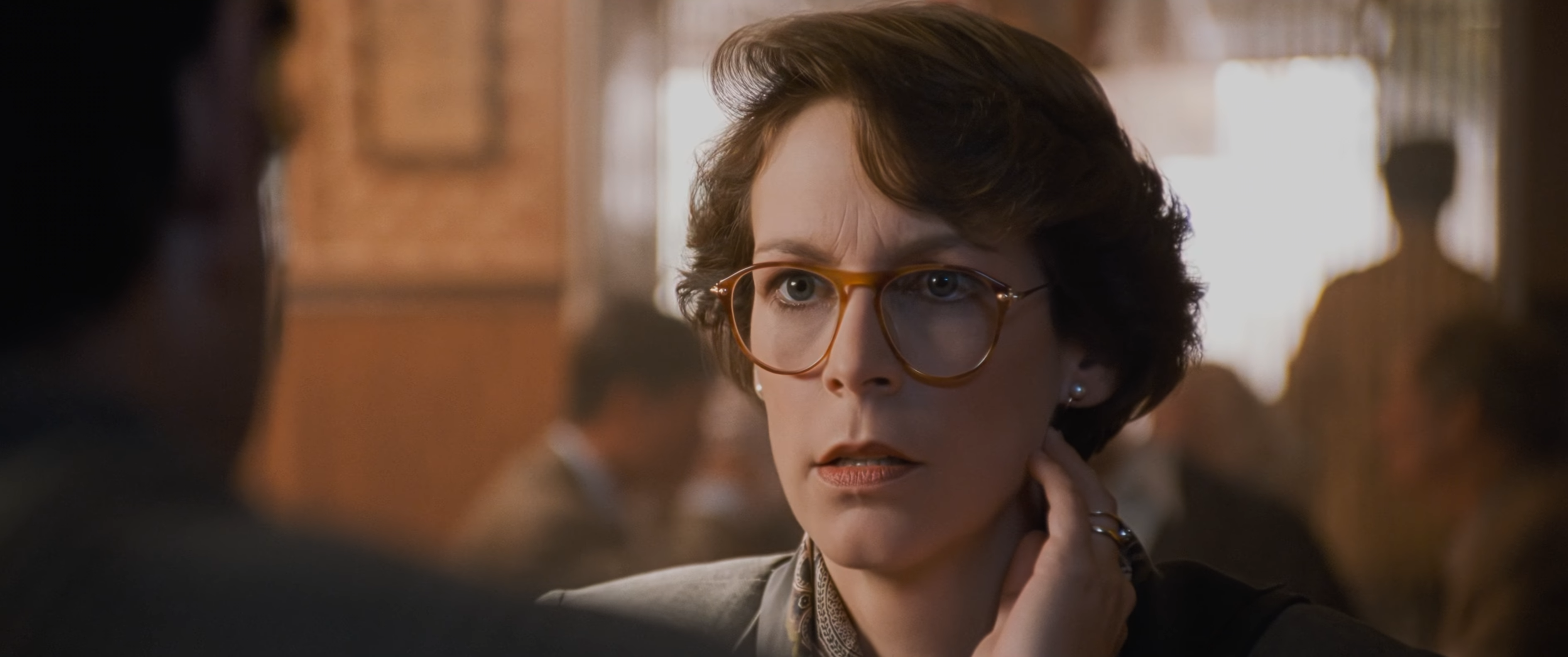 : A woman wearing glasses speaks to someone in a warmly lit restaurant.