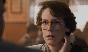 : A woman wearing glasses speaks to someone in a warmly lit restaurant.