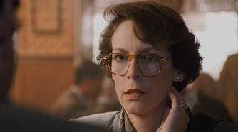 : A woman wearing glasses speaks to someone in a warmly lit restaurant.