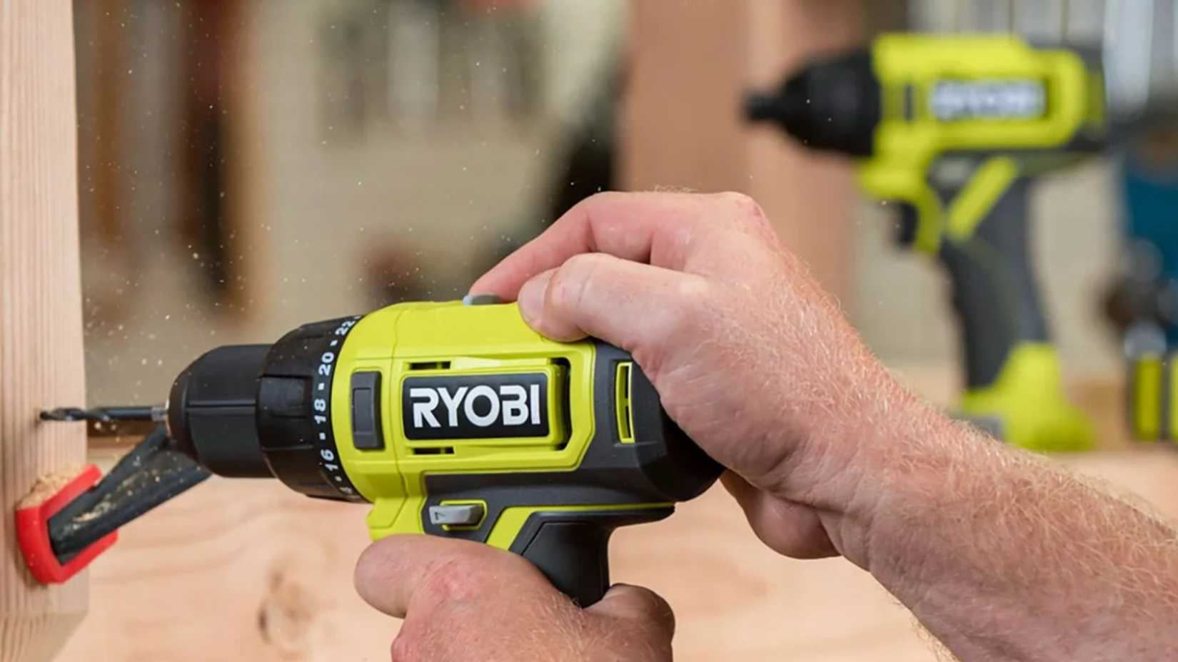 A close up to a drill drilling through wood next to another drill in Ryobi