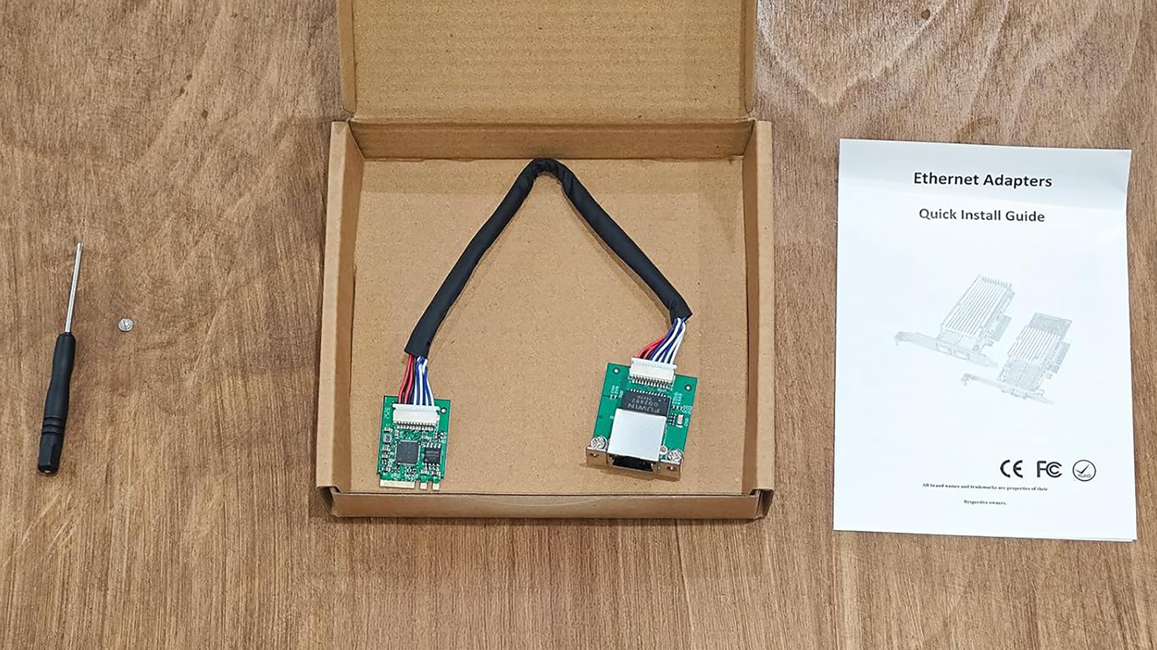 An M.2 NIC in a box surrounded by a screw, a screwdriver, and a install guide. 