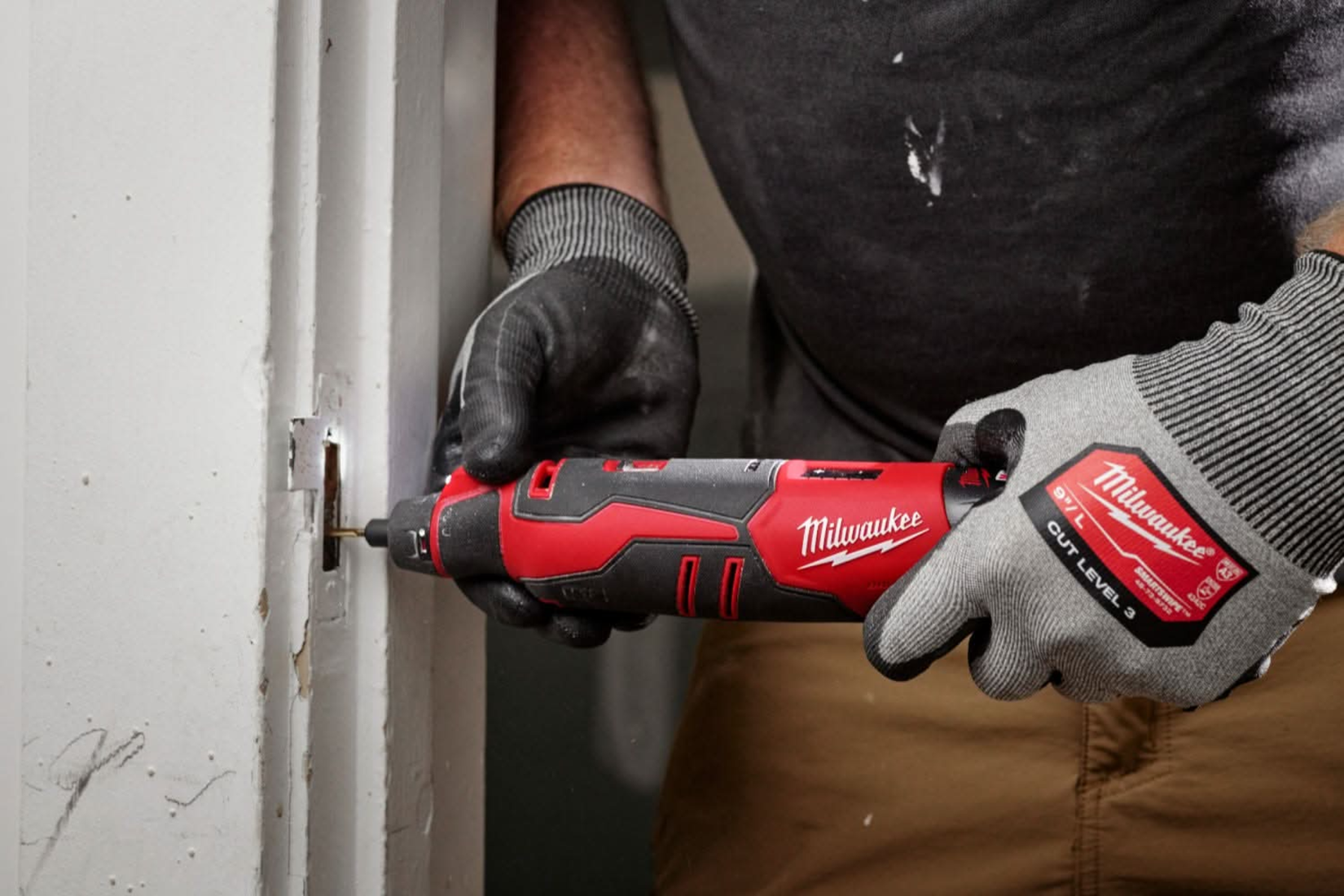 A man using Milwaukee's M12 rotary tool to drill out a door frame.