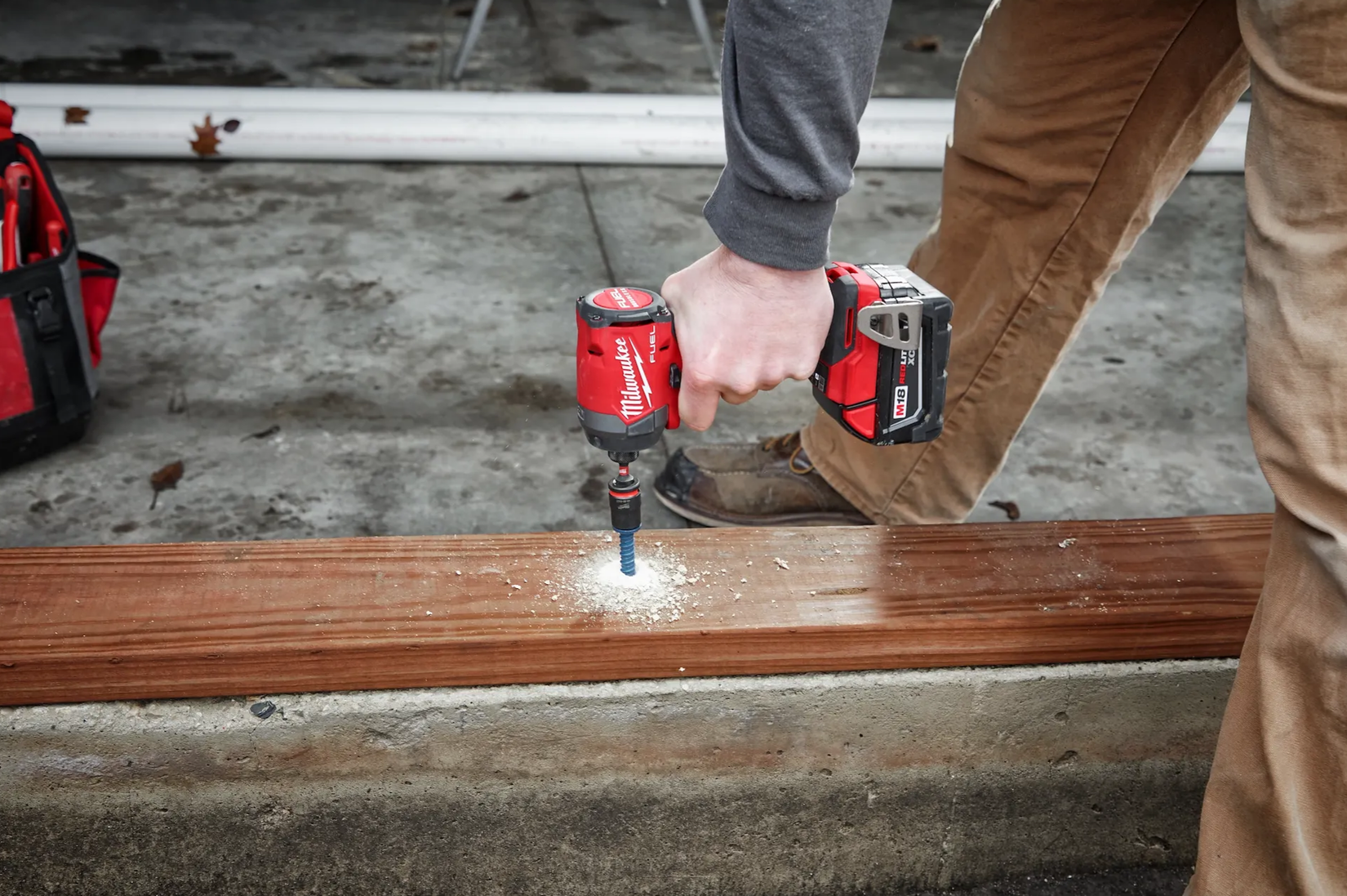 Milwaukee M18 FUEL 1/4" impact driver 2953-20 driving a screw through wood into concrete