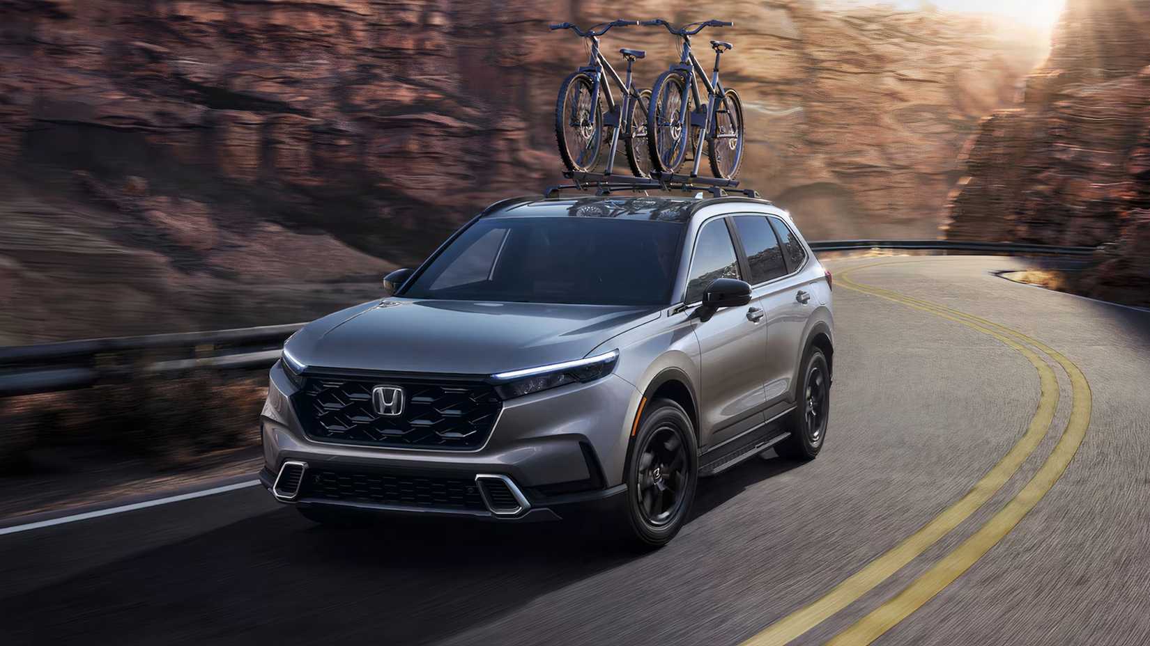 Dynamic front 3/4 shot of a gray 2025 Honda CR-V Hybrid with bikes mounted on the roof.