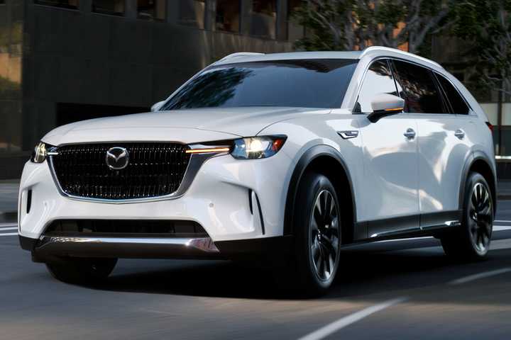 Dynamic front 3/4 shot fo a white 2025 Mazda CX-90 driving in a city.