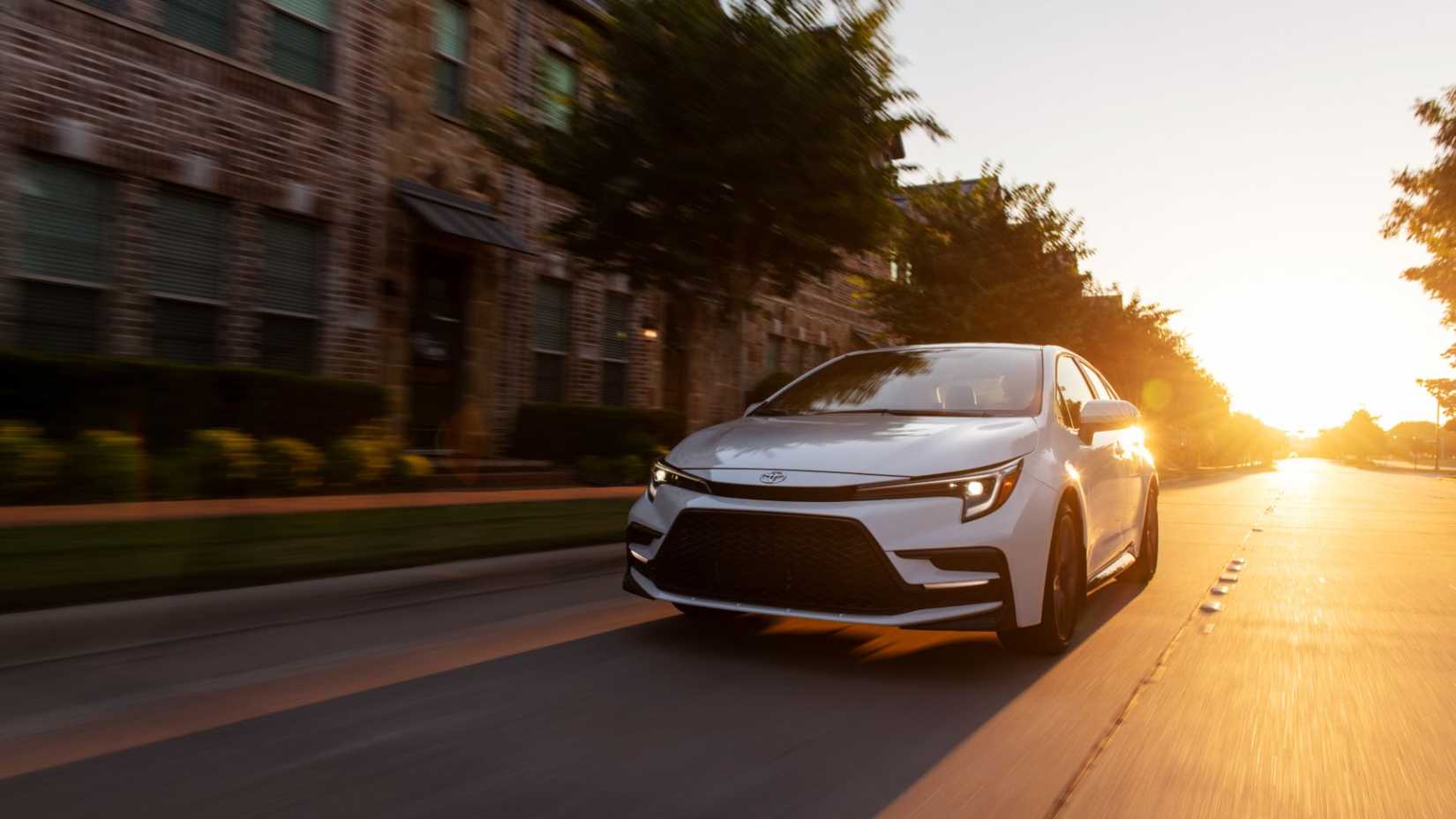 2025 Toyota Corolla Sedan White Front View Driving in the City and Sunset