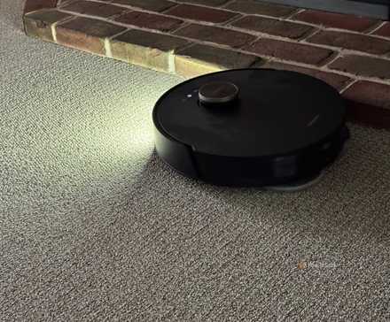 Showing a DreameBot L20 Ultra robot vacuum cleaning with its front light on.
