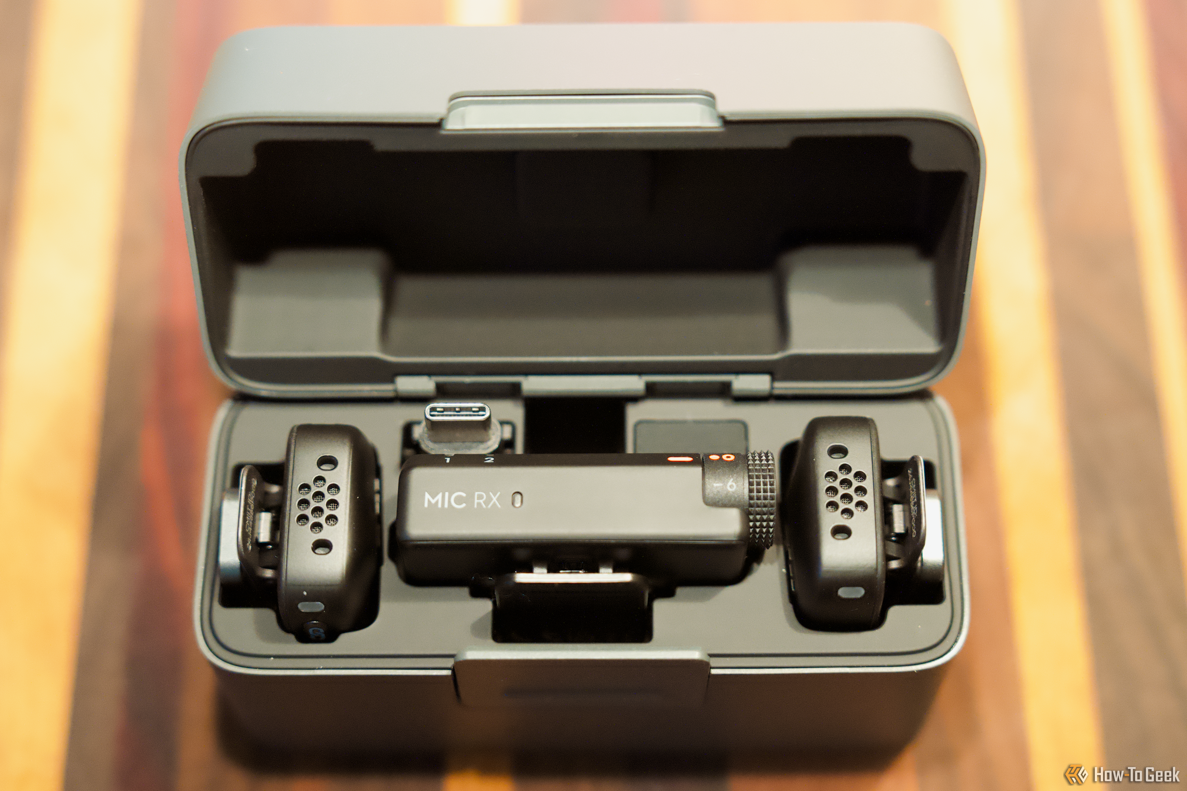 The DJI Mic Mini case complete with the two mics, receiver, and accessoreis sits on a wooden table. 