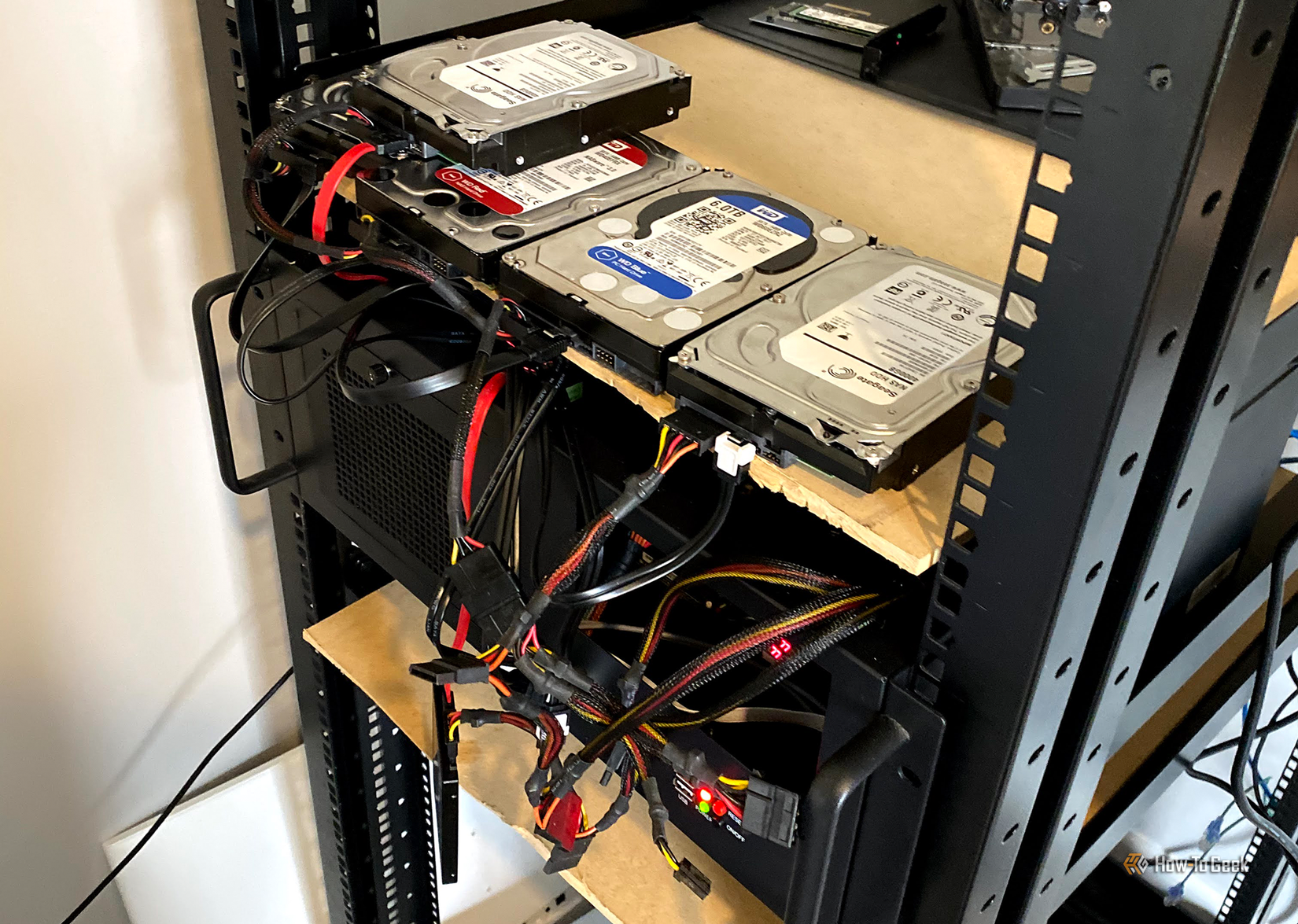 Hard drives sitting on a shelf with cables going everywhere plugged into a rack-mounted computer.