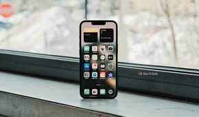 iPhone 16e in front of window displaying its Home screen.