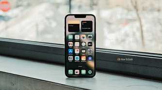 iPhone 16e in front of window displaying its Home screen.