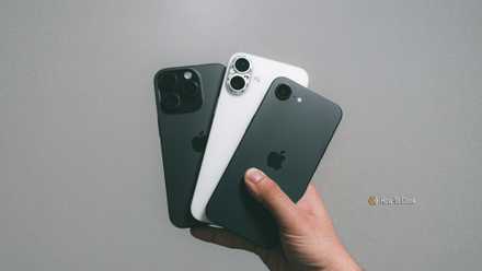 iPhone 16e with iPhone 16 Plus and iPhone 16 Pro in hand against grey wall.