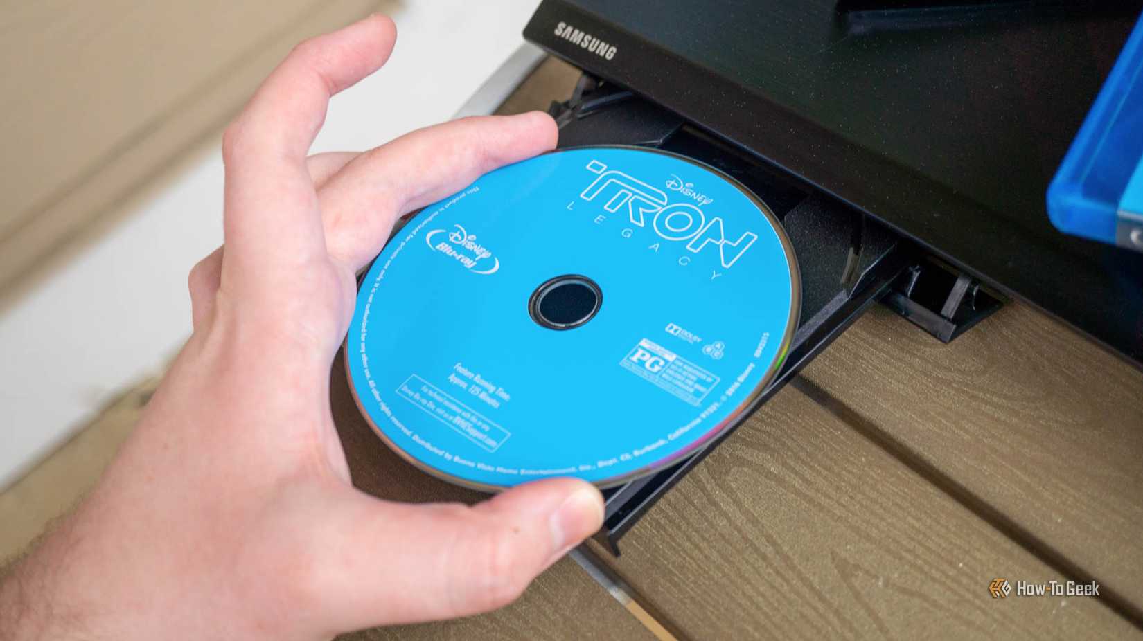 Person's hand putting a Blu-ray disc in Blu-ray player.