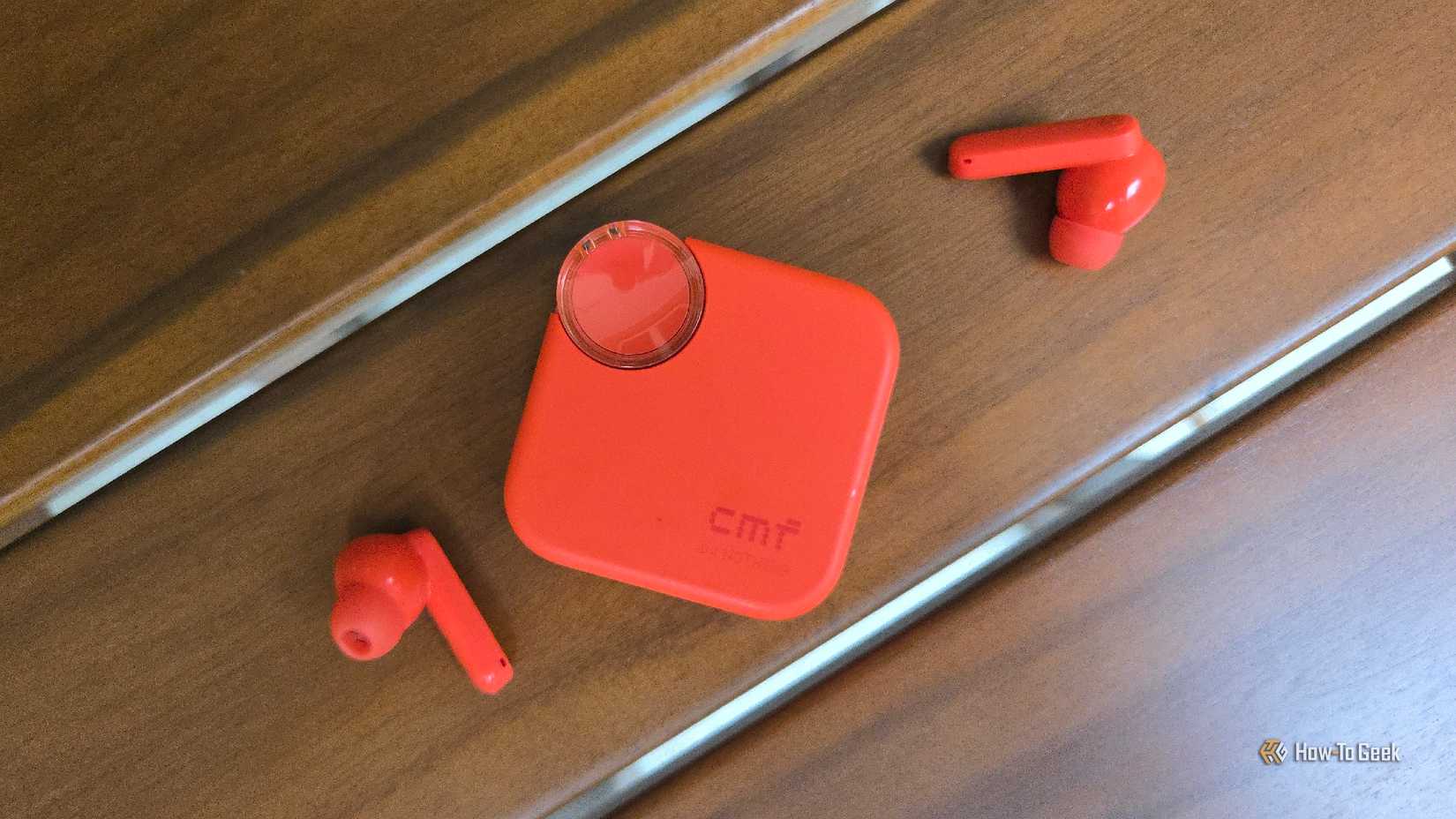 Two CMF Buds 2 buds on a table next to their case.