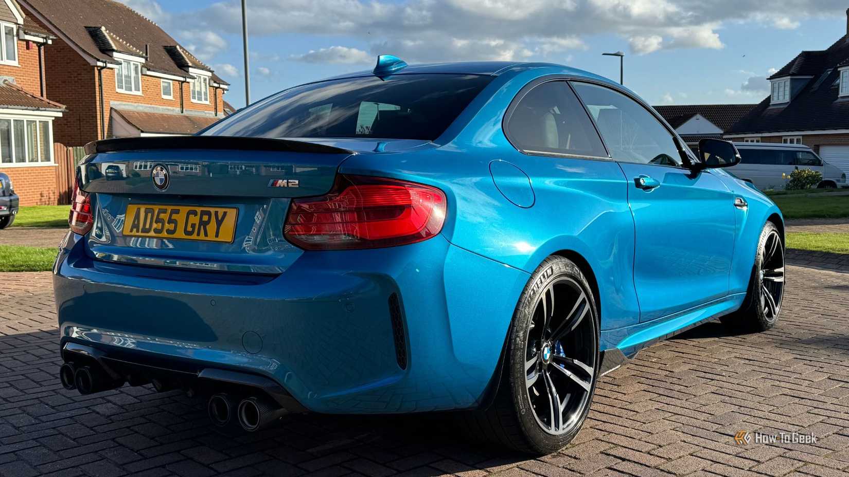 Static rear 3/4 shot of a blue 2018 BMW M2 with houses in the background.