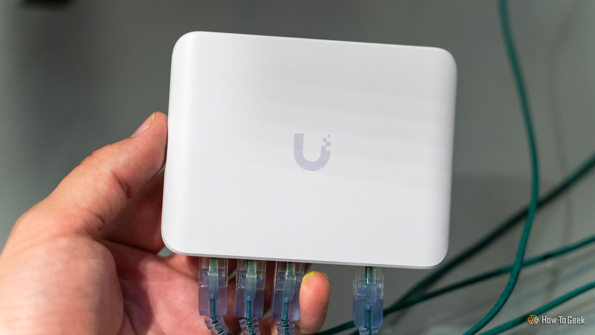 O switch Ethernet Unifi Flex Mini 2.5G com cabos Ethernet conectados e segurado com a mão.