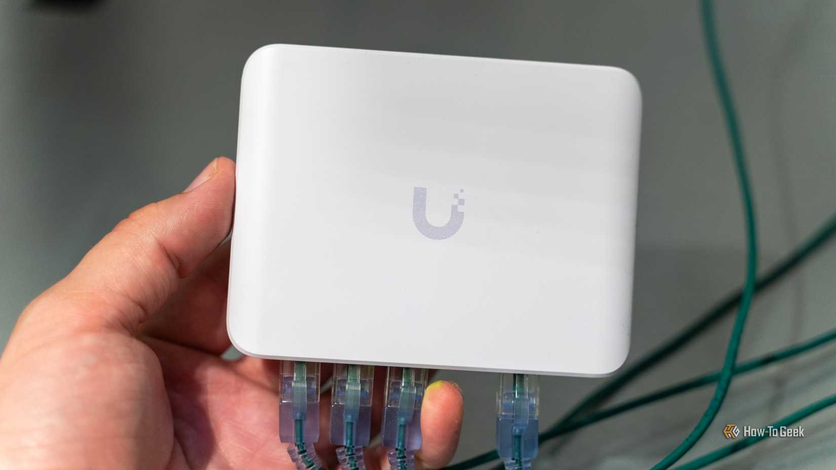 The Unifi Flex Mini 2.5G Ethernet Switch with plugged-in Ethernet cables is held in one hand.