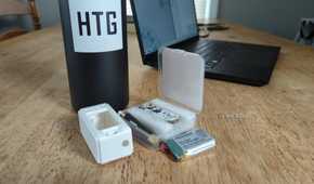 A MakerHawk LoRa radio kit with the board, case, and battery visible in front of a laptop and water bottle with the How-To Geek logo on it.