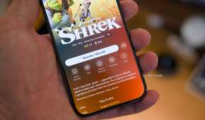 An iPhone 15 Pro held in a hand showing the Plex mobile app with the download icon visible on the Shrek movie.