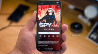 An iPhone 15 Pro held in a hand over a desk with the Spy Kids movie shown on the Plex mobile app.