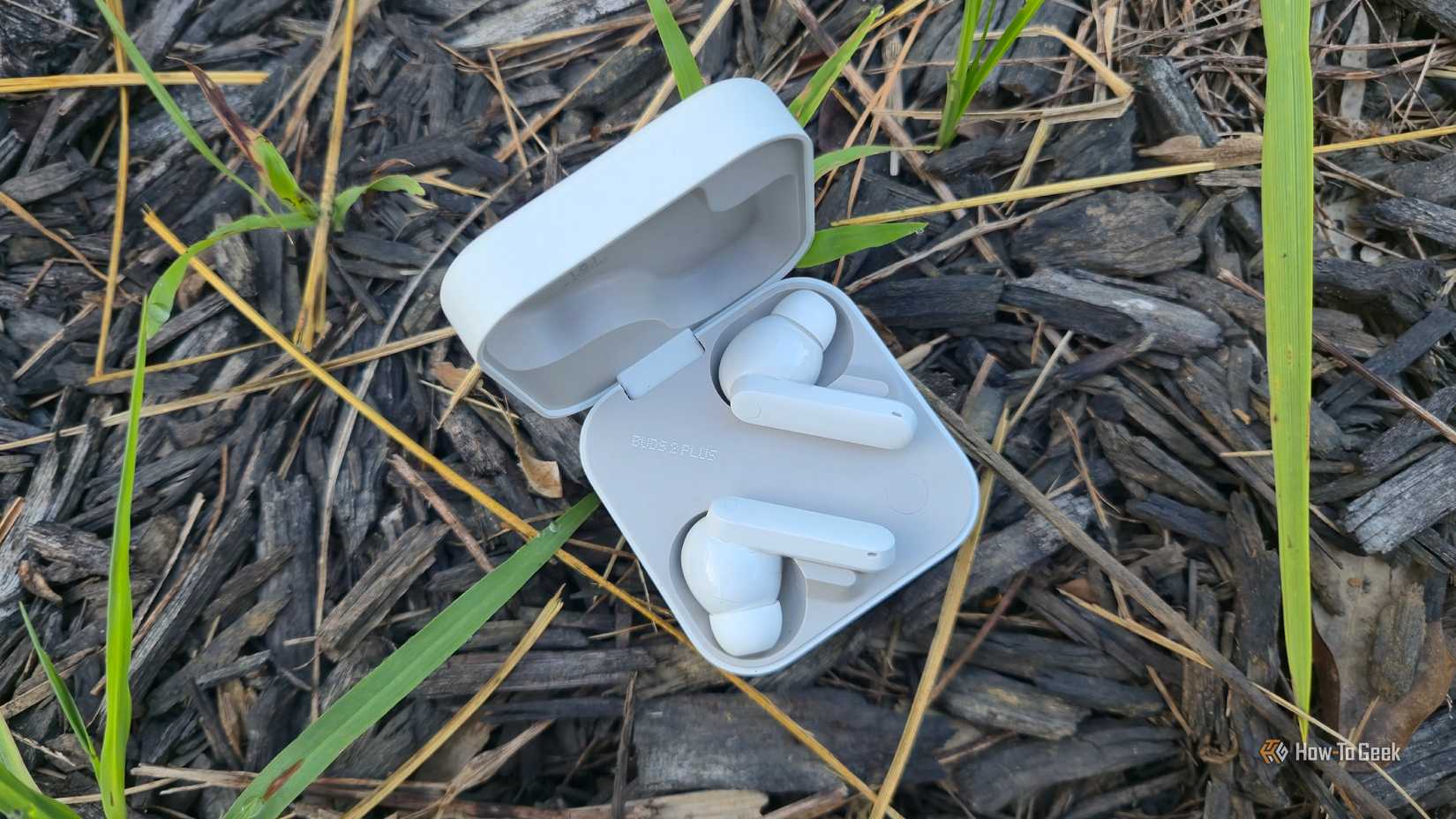 CMF Buds 2 Pro en un estuche entre mantillo y briznas de graaa.