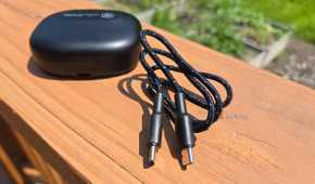 Included USB-C cable next to the case for JLab Epic Open Sport on a deck railing.