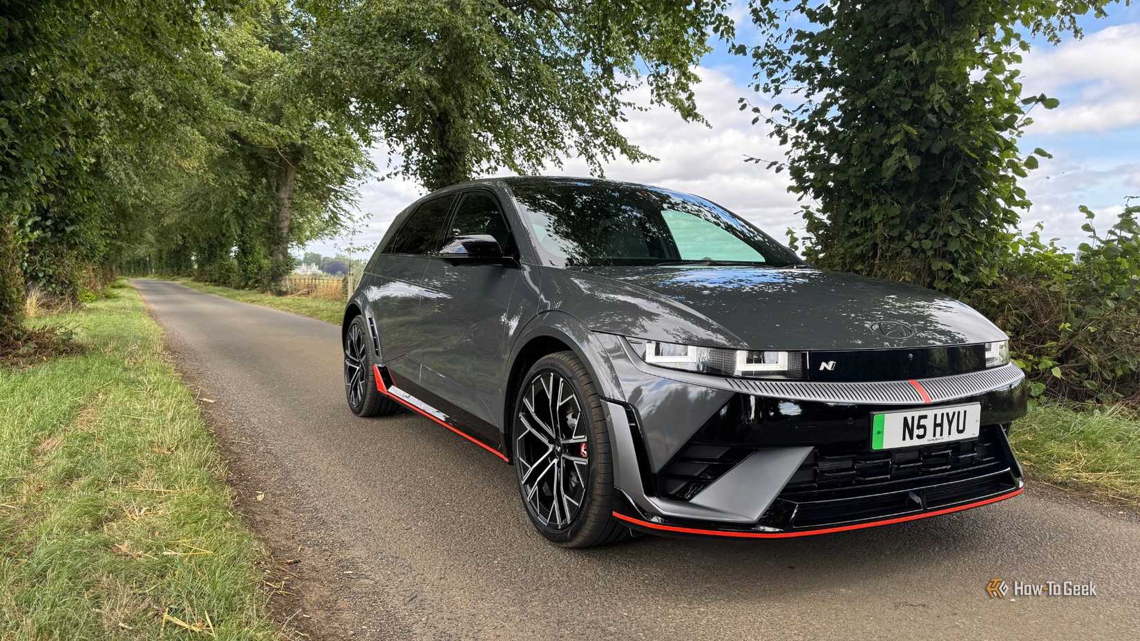 Static front 3/4 shot of a gray 2025 Hyundai Ioniq 5 N parked on a country road lined by trees.