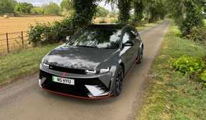 Static front 3/4 shot of a gray 2025 Hyundai Ioniq 5 N parked on a country road lined by trees.